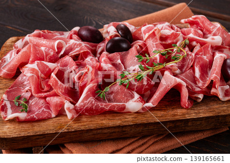 Freshly cut dried meat, served with olives and herbs, on a wooden chopping board, no people, 139165661