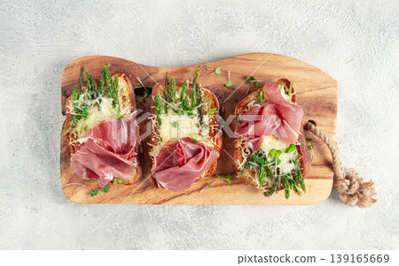 open sandwiches with asparagus and prosciutto, with cheese, breakfast, on a wooden serving board, 139165669