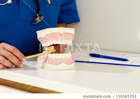 A dentist in a blue uniform demonstrates the correct technique of brushing teeth, on a model, in a clinical setting, A dentist in a blue uniform demonstrates the correct technique of brushing teeth, on a model, in a clinical setting, 139165701