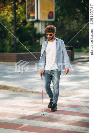 Wearing casual clothes, having a walk. Blind man with white cane and sunglasses is in the city Wearing casual clothes, having a walk. Blind man with white cane and sunglasses is in the city 139165787