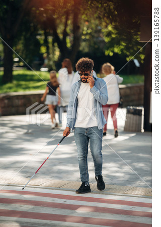 Having conversation by phone. Blind man with white cane and sunglasses is in the city Having conversation by phone. Blind man with white cane and sunglasses is in the city 139165788
