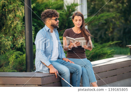 Interesting information. Woman is with blind man, sitting outdoors and reading book Interesting information. Woman is with blind man, sitting outdoors and reading book 139165805