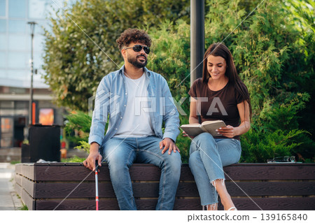 Interesting information. Woman is with blind man, sitting outdoors and reading book 139165840