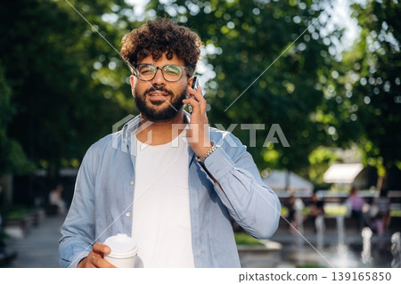 Paper cup in right hand and smartphone in left one. Handsome man is outdoors in the city Paper cup in right hand and smartphone in left one. Handsome man is outdoors in the city 139165850