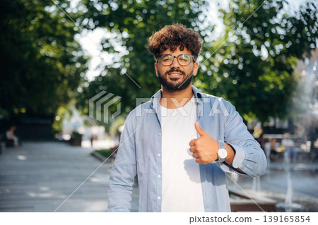 Looking at the camera, standing. Handsome man is outdoors in the city Looking at the camera, standing. Handsome man is outdoors in the city 139165854