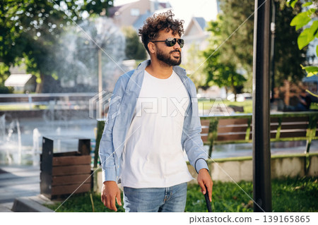 Having a walk, using cane stick. Blind man with white cane and sunglasses is in the city 139165865