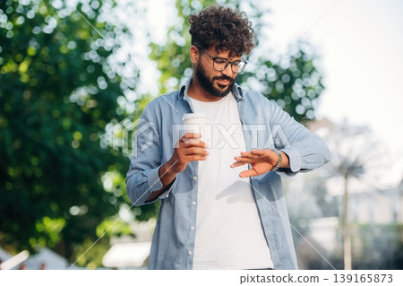 Checks the time, looks at his wristwatch. Handsome man is outdoors in the city Checks the time, looks at his wristwatch. Handsome man is outdoors in the city 139165873