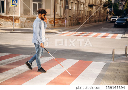 Side view, walking. Blind man with white cane and sunglasses is in the city 139165894