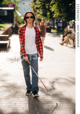 Front view, walking. Blind young guy is in the town outdoors 139166151