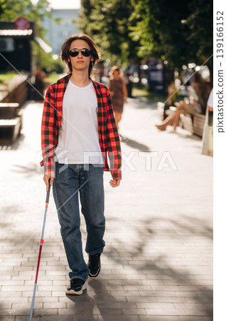 White cane is in hand. Blind young guy is in the town outdoors 139166152