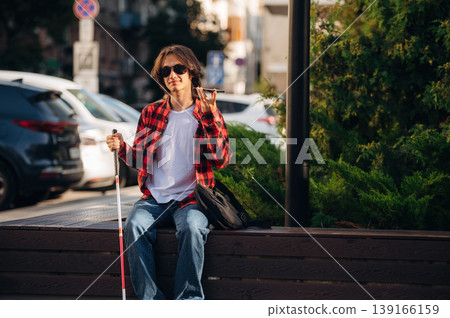 Smartphone in hand, talking. Blind young guy is in the town outdoors Smartphone in hand, talking. Blind young guy is in the town outdoors 139166159