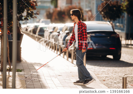 The practical use of white cane. Blind young guy is in the town outdoors The practical use of white cane. Blind young guy is in the town outdoors 139166166
