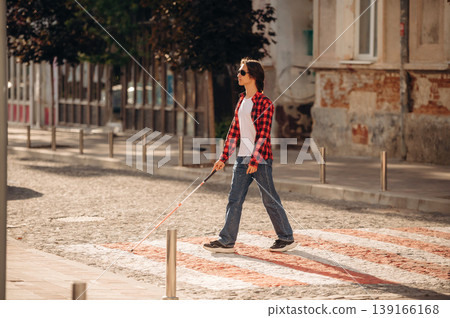View from the side, walking. Blind young guy is in the town outdoors View from the side, walking. Blind young guy is in the town outdoors 139166168