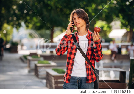 In red checkered shirt. Young student is having a walk in the town In red checkered shirt. Young student is having a walk in the town 139166216