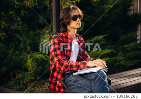 Reading the book using Braille technique. Blind young guy is in the town outdoors Reading the book using Braille technique. Blind young guy is in the town outdoors 139166268