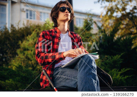 Reading the book using Braille technique. Blind young guy is in the town outdoors Reading the book using Braille technique. Blind young guy is in the town outdoors 139166270