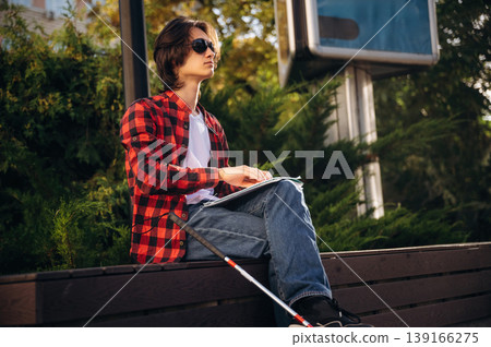 Technique of Braille reading. Blind young guy is in the town outdoors Technique of Braille reading. Blind young guy is in the town outdoors 139166275