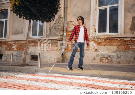 Crossing the road. Blind young guy is in the town outdoors Crossing the road. Blind young guy is in the town outdoors 139166290