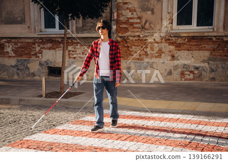 Crossing the road. Blind young guy is in the town outdoors Crossing the road. Blind young guy is in the town outdoors 139166291