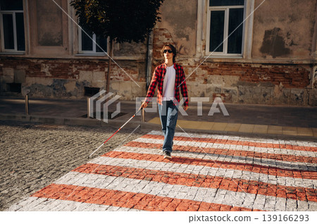 Crossing the road. Blind young guy is in the town outdoors Crossing the road. Blind young guy is in the town outdoors 139166293