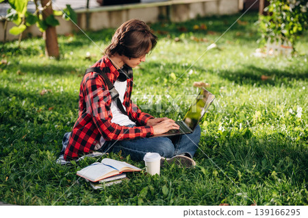 Laptop is on legs. Male student is in the public park outdoors 139166295