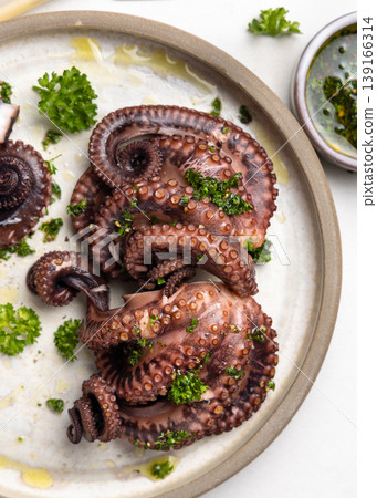 Boiled octopus on ceramic plate with olive oil and parsley dressing top view. Seafood appetizer 139166314