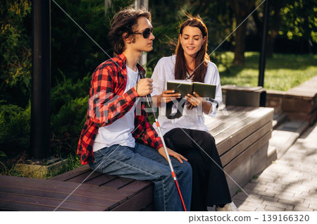 Woman is reading the book for blind guy, sitting outdoors 139166320