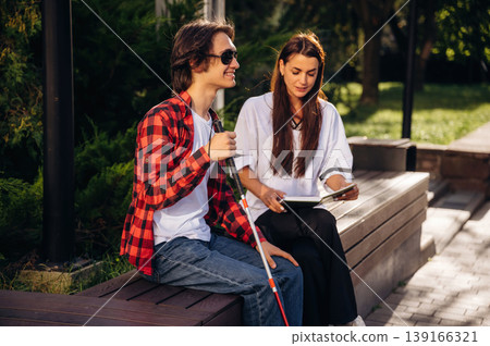Smiling, enjoying the story. Woman is reading the book for blind guy, sitting outdoors 139166321