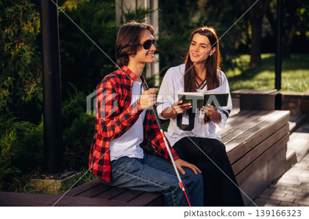 Smiling, enjoying the story. Woman is reading the book for blind guy, sitting outdoors Smiling, enjoying the story. Woman is reading the book for blind guy, sitting outdoors 139166323
