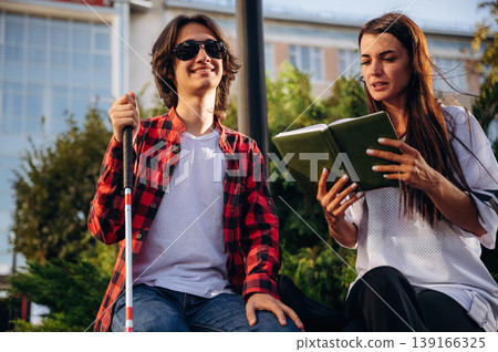 Smiling, enjoying the story. Woman is reading the book for blind guy, sitting outdoors Smiling, enjoying the story. Woman is reading the book for blind guy, sitting outdoors 139166325