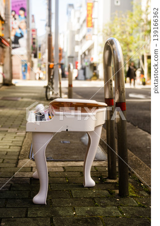 A white toy piano placed next to a bollard on a city sidewalk. A white toy piano placed next to a bollard on a city sidewalk. 139166362
