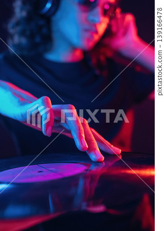 DJ is with vinyl. Guy is indoors at night with neon lighting DJ is with vinyl. Guy is indoors at night with neon lighting 139166478