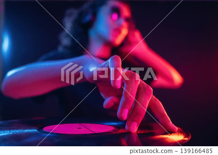Vinyl record manipulation by DJ. Guy is indoors at night with neon lighting 139166485