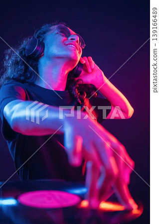 Night club, DJ is with vinyl. Guy is indoors at night with neon lighting Night club, DJ is with vinyl. Guy is indoors at night with neon lighting 139166489