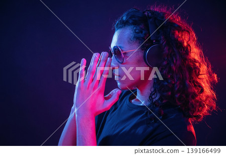 Long hair, headphones, side view. Guy is indoors at night with neon lighting Long hair, headphones, side view. Guy is indoors at night with neon lighting 139166499