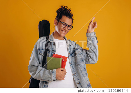 Guitar backpack on back and notepads in hand. Young guy is against yellow background Guitar backpack on back and notepads in hand. Young guy is against yellow background 139166544