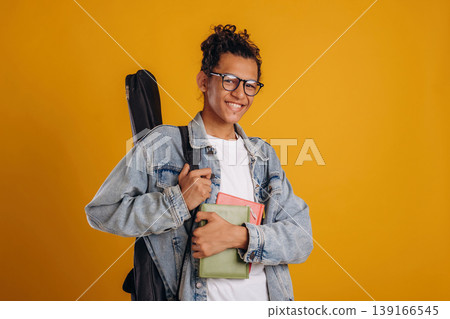 Guitar backpack on back and notepads in hand. Young guy is against yellow background Guitar backpack on back and notepads in hand. Young guy is against yellow background 139166545