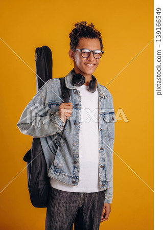 Black guitar bag on back. Young guy is against yellow background Black guitar bag on back. Young guy is against yellow background 139166549