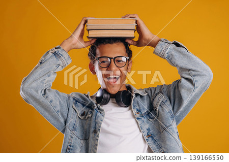 Student is holding books over the head. Young guy is against yellow background 139166550
