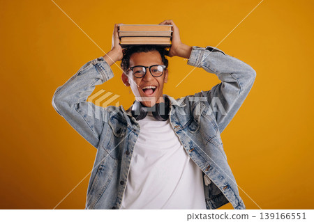 Student is holding books over the head. Young guy is against yellow background Student is holding books over the head. Young guy is against yellow background 139166551