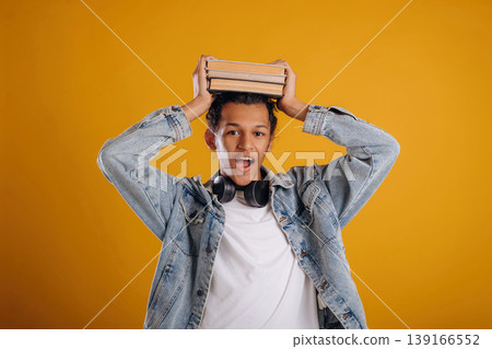 Student is holding books over the head. Young guy is against yellow background 139166552