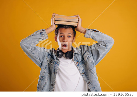 Student is holding books over the head. Young guy is against yellow background Student is holding books over the head. Young guy is against yellow background 139166553