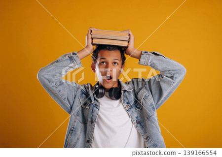 Student is holding books over the head. Young guy is against yellow background 139166554