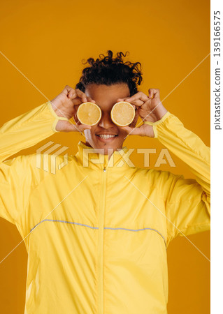 Sliced lemons by eyes, holding healthy food. Young guy is against yellow background Sliced lemons by eyes, holding healthy food. Young guy is against yellow background 139166575