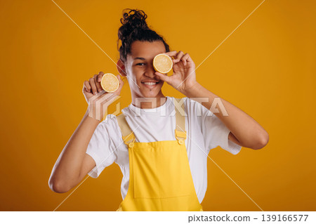 Sliced lemons by eyes, holding healthy food. Young guy is against yellow background Sliced lemons by eyes, holding healthy food. Young guy is against yellow background 139166577