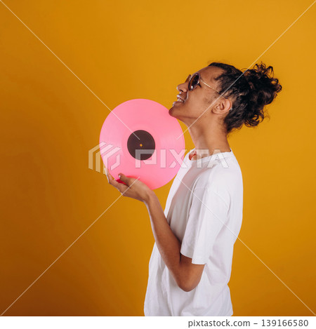 Pink colored vinyl record, music lover. Young guy is against yellow background Pink colored vinyl record, music lover. Young guy is against yellow background 139166580