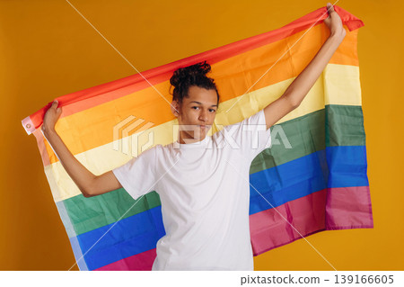 LGBT flag is in hands, supporting the pride community. Young guy is against yellow background LGBT flag is in hands, supporting the pride community. Young guy is against yellow background 139166605