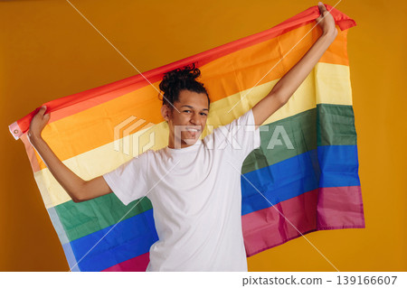 LGBT flag is in hands, supporting the pride community. Young guy is against yellow background 139166607