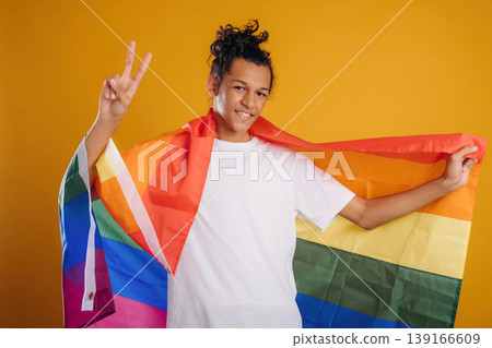 LGBT flag is in hands, supporting the pride community. Young guy is against yellow background LGBT flag is in hands, supporting the pride community. Young guy is against yellow background 139166609
