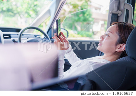A woman passing the time in the driver's seat of a car. 139166637